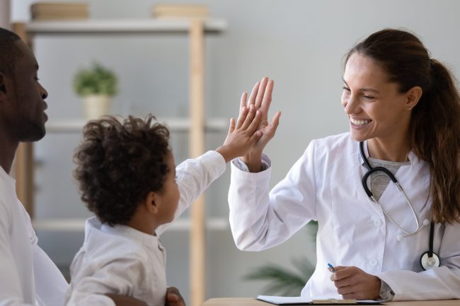 Smiling young female pediatrician give high five to little african American boy at consultation in clinic, happy woman doctor consult biracial toddler kid in hospital. Children healthcare concept